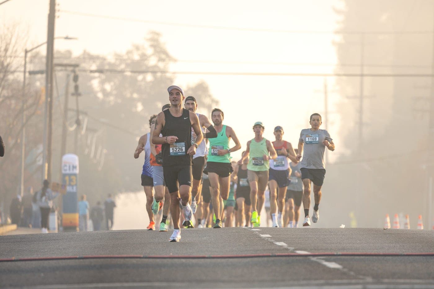 A pack of road-race runners with bibs on a foggy morning street