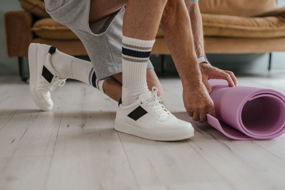 A person in white crew socks and sneakers kneeling on a wood floor